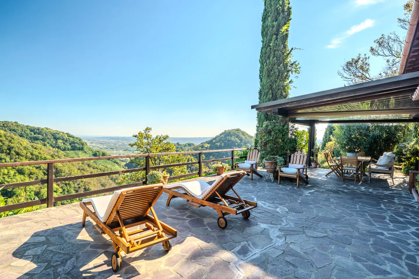 Outdoor patio with two lounge chairs, a table and chairs, and a view of rolling hills under a blue sky.