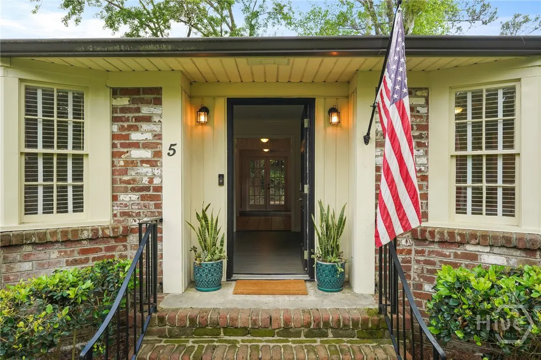 Front entrance of a brick house with an open black door, American flag, and potted plants.