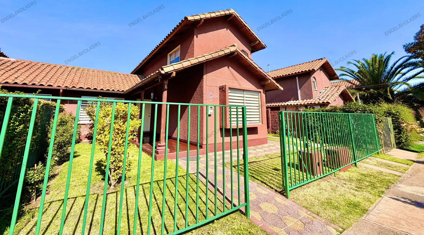Red two-story house with a brown roof and green fence on a sunny day.