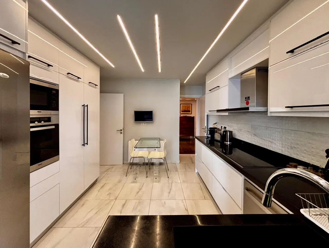 Bright, modern kitchen with white cabinets, black countertops, and stainless steel appliances. Linear lighting illuminates the space.