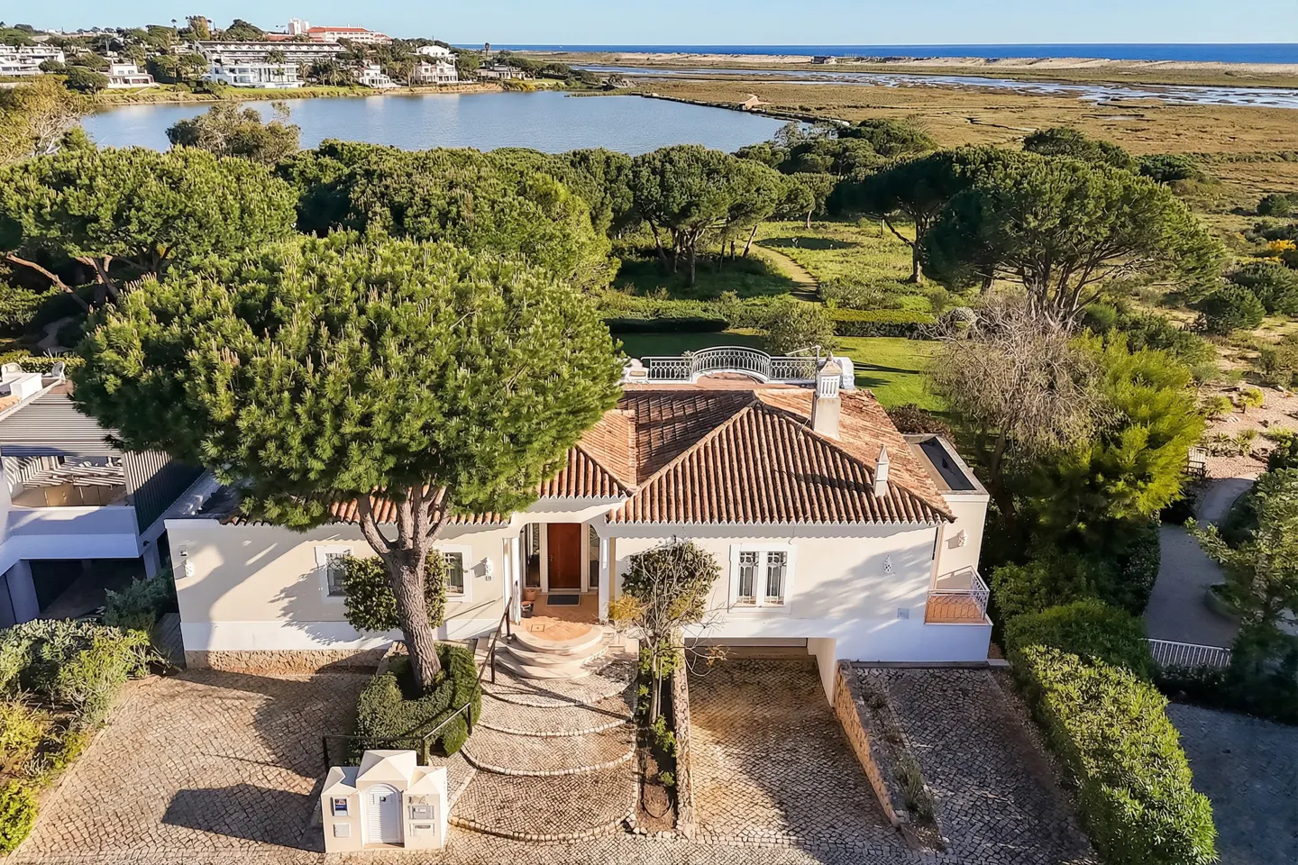 Aerial view of a white house with a red tile roof, surrounded by green trees, with a lake and marsh in the background.