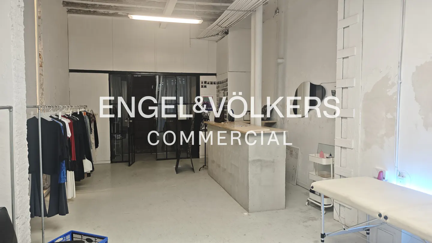 A commercial space with white walls, a concrete counter, and clothing racks. A treatment table is visible in the foreground.