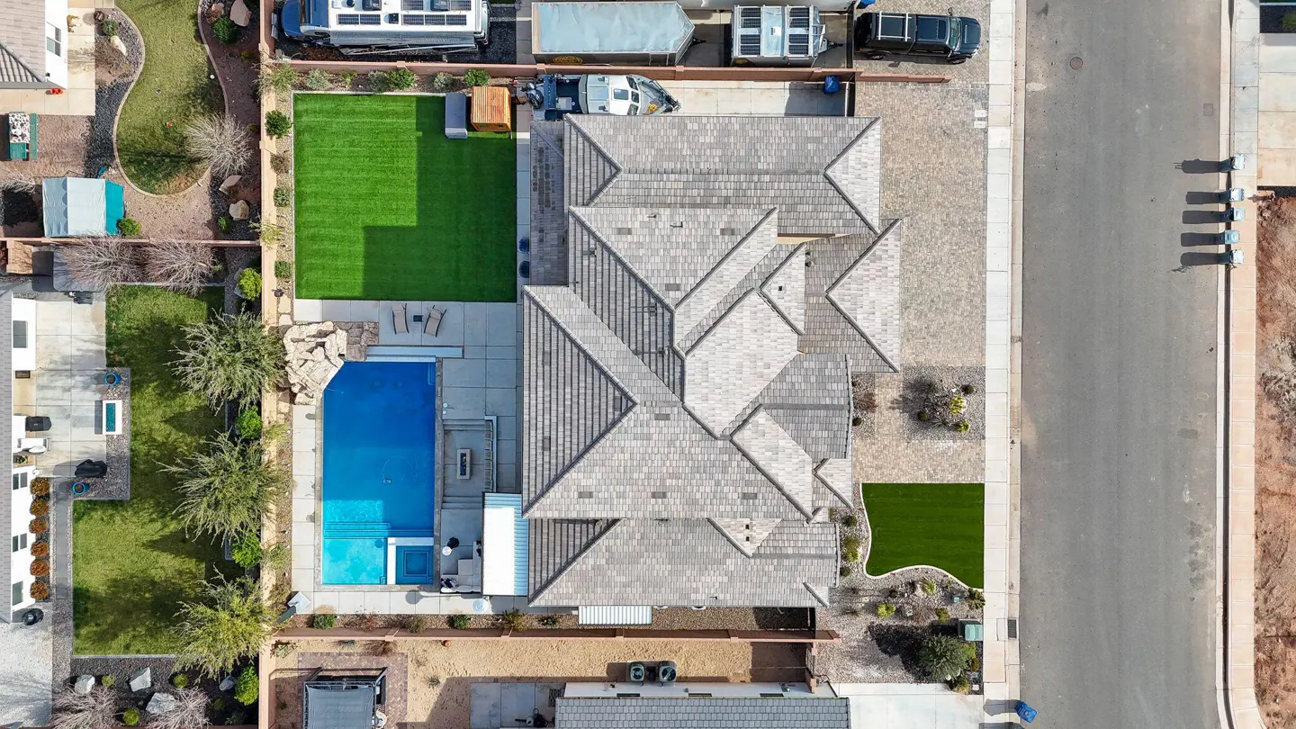 Aerial view of a house with a gray roof, a blue pool, and a green lawn, next to a street.