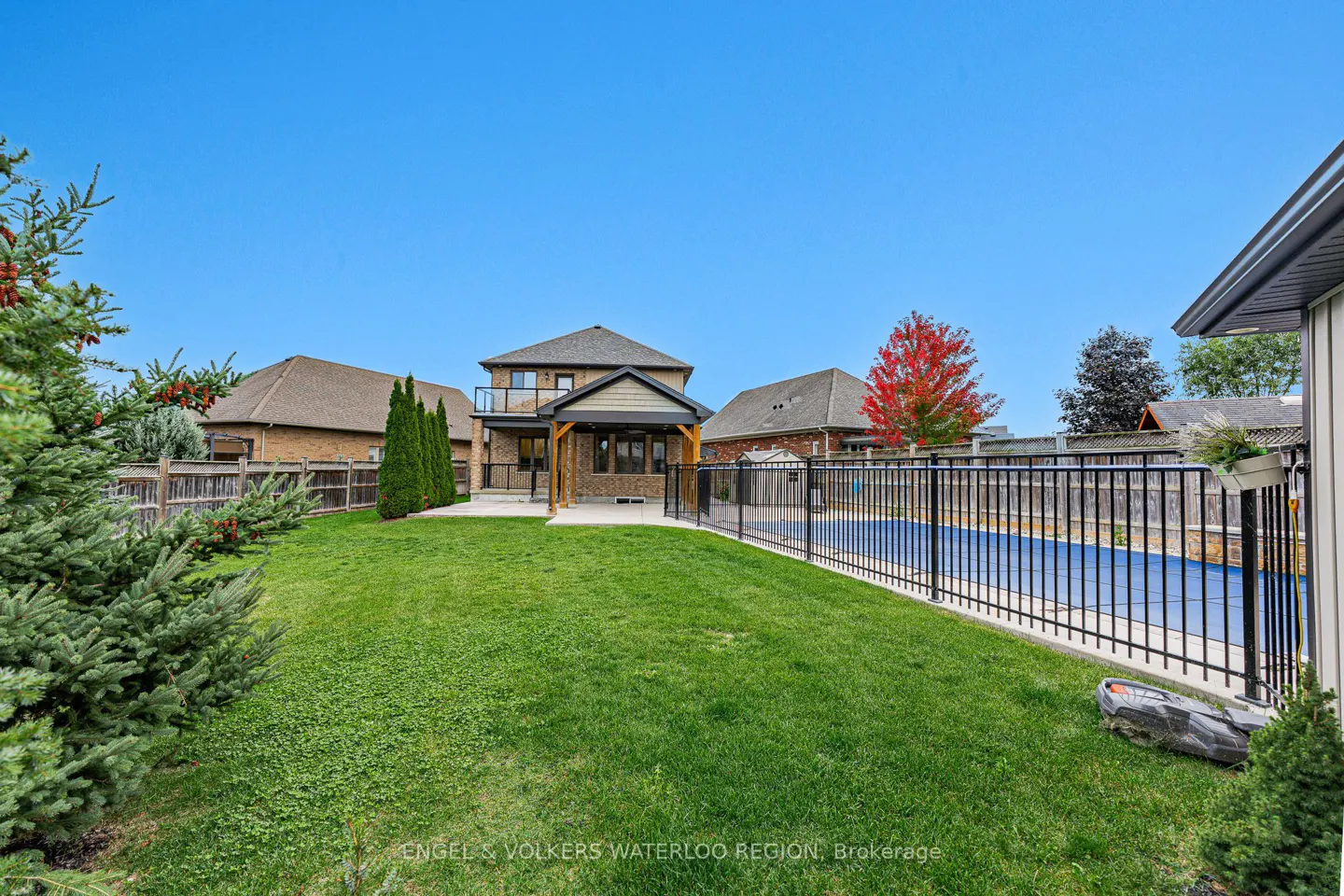A backyard with a green lawn, a black metal fence around a pool, and a two-story house with a balcony.