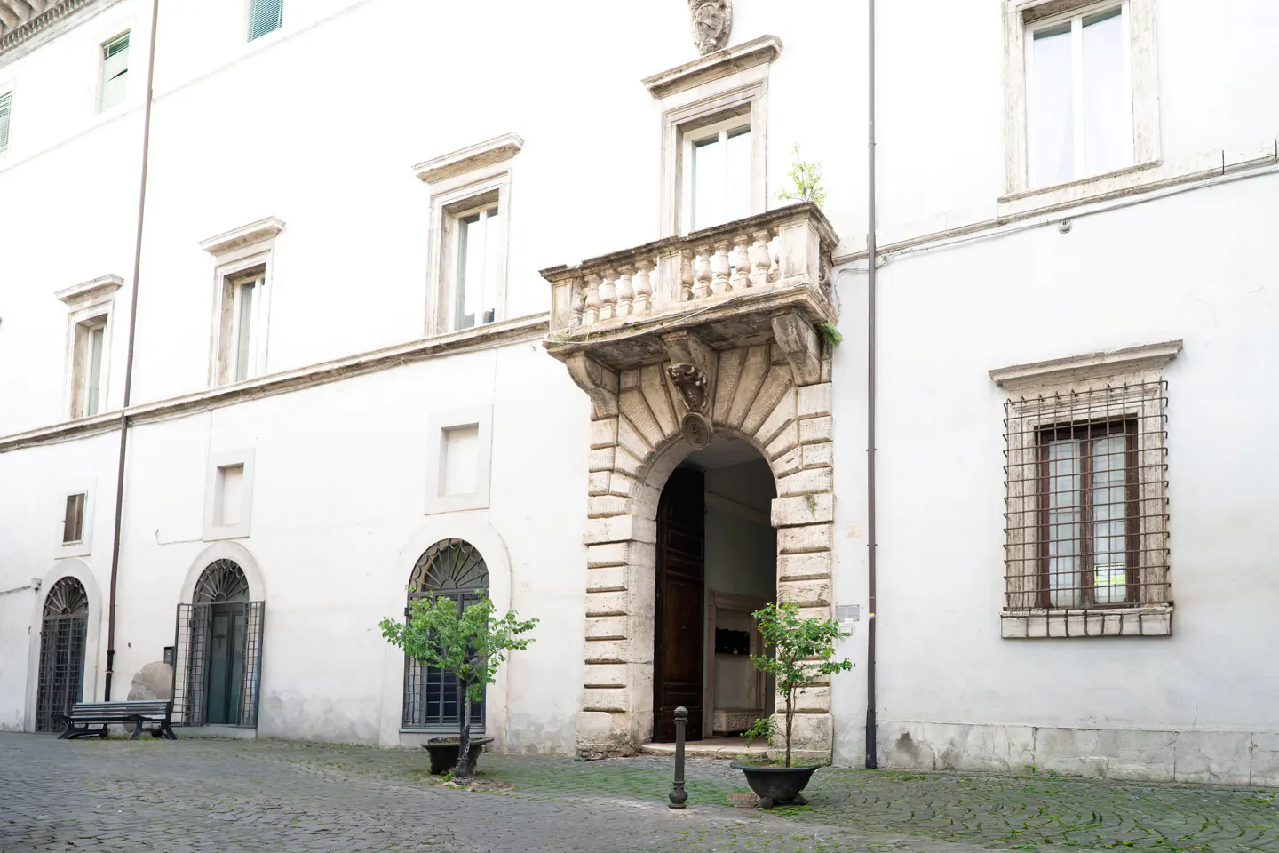 Exterior of a white building with arched doorway, balcony, windows, and cobblestone street.