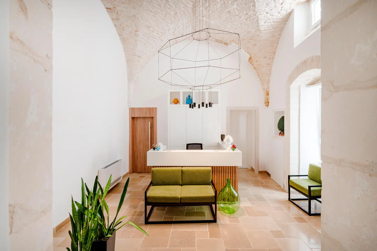 Bright lobby with arched ceilings, a white reception desk, and green seating. A geometric chandelier hangs above.