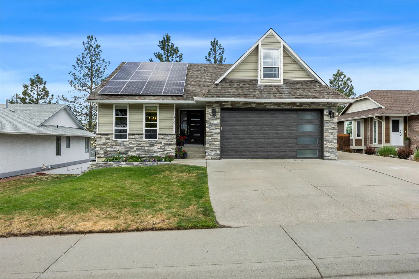 A one-story house with solar panels, a gray garage door, and a green lawn on a sunny day.