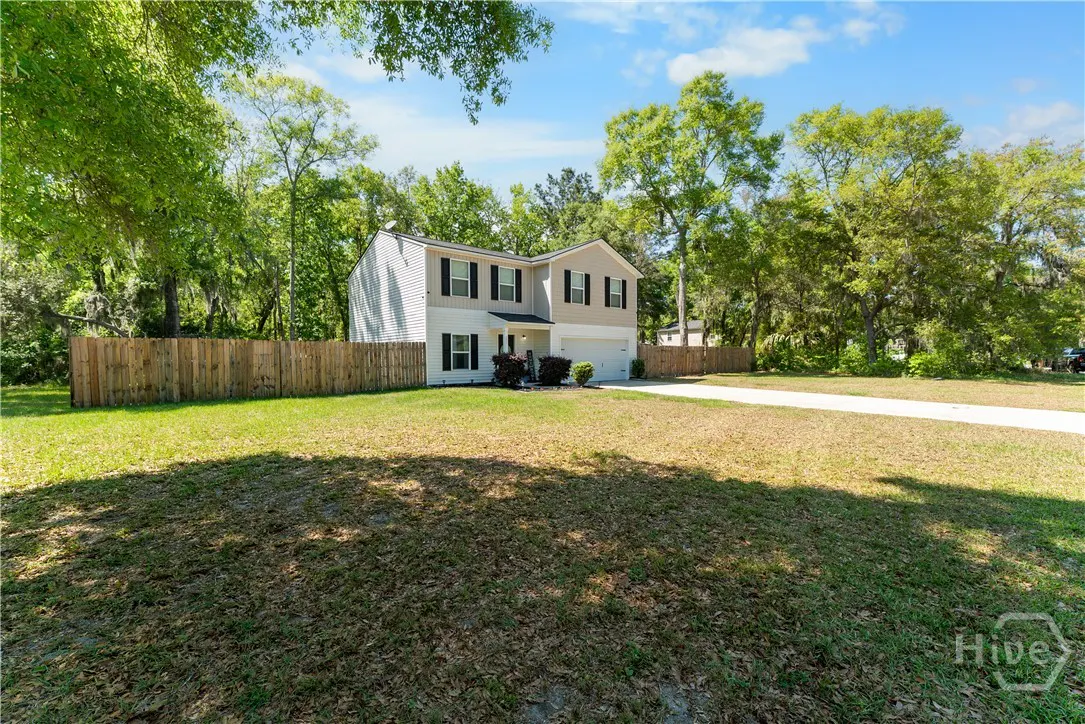 Two-story house with white and beige siding, black shutters, and a wooden fence, surrounded by green trees and grass.