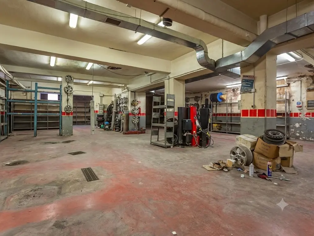 Spacious, industrial-style garage interior with red concrete floors, metal shelving, car parts, and exposed ductwork.