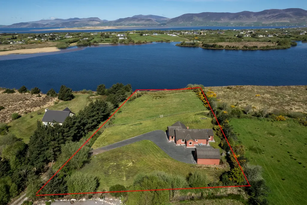Aerial view of a property outlined in red, featuring a red brick house, green lawn, and a lake with mountains in the background.