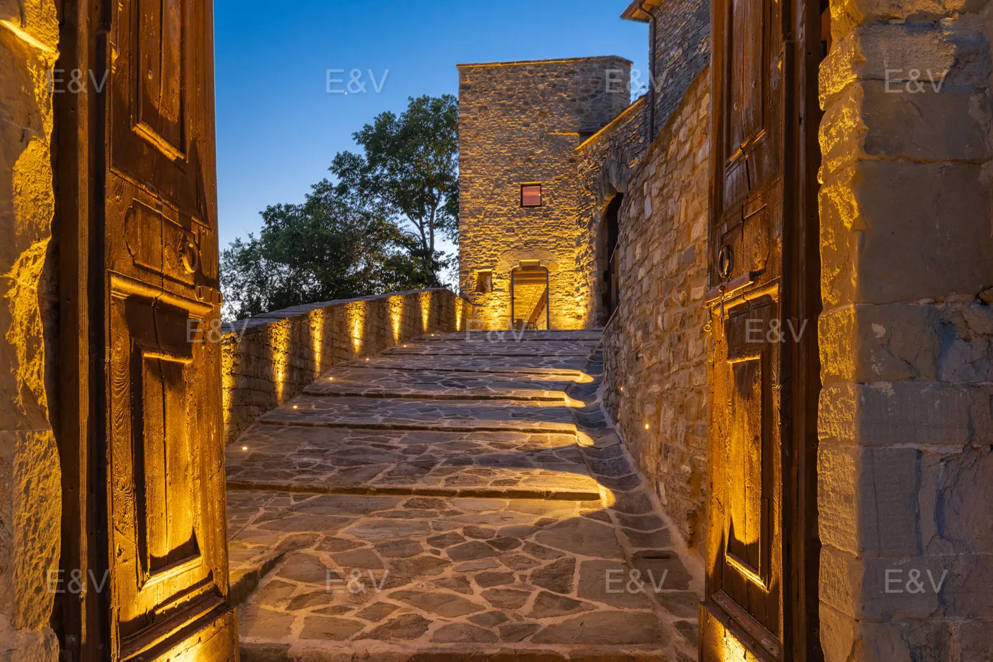 Stone steps lead up to a stone building, illuminated by warm lights, framed by open wooden doors.