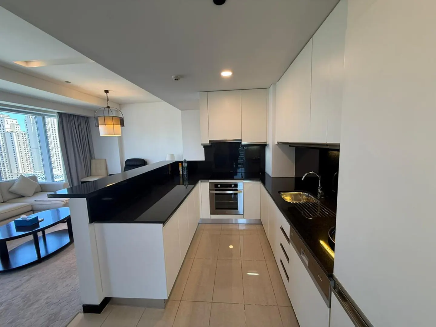 A modern kitchen with white cabinets, black countertops, and stainless steel appliances. A living room is visible in the background.