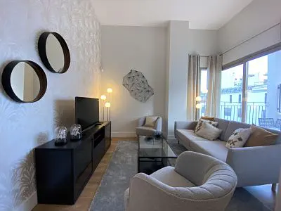 Living room with gray sofa, chair, and rug. Black TV stand with TV and round mirrors on the wall. Large window with curtains.