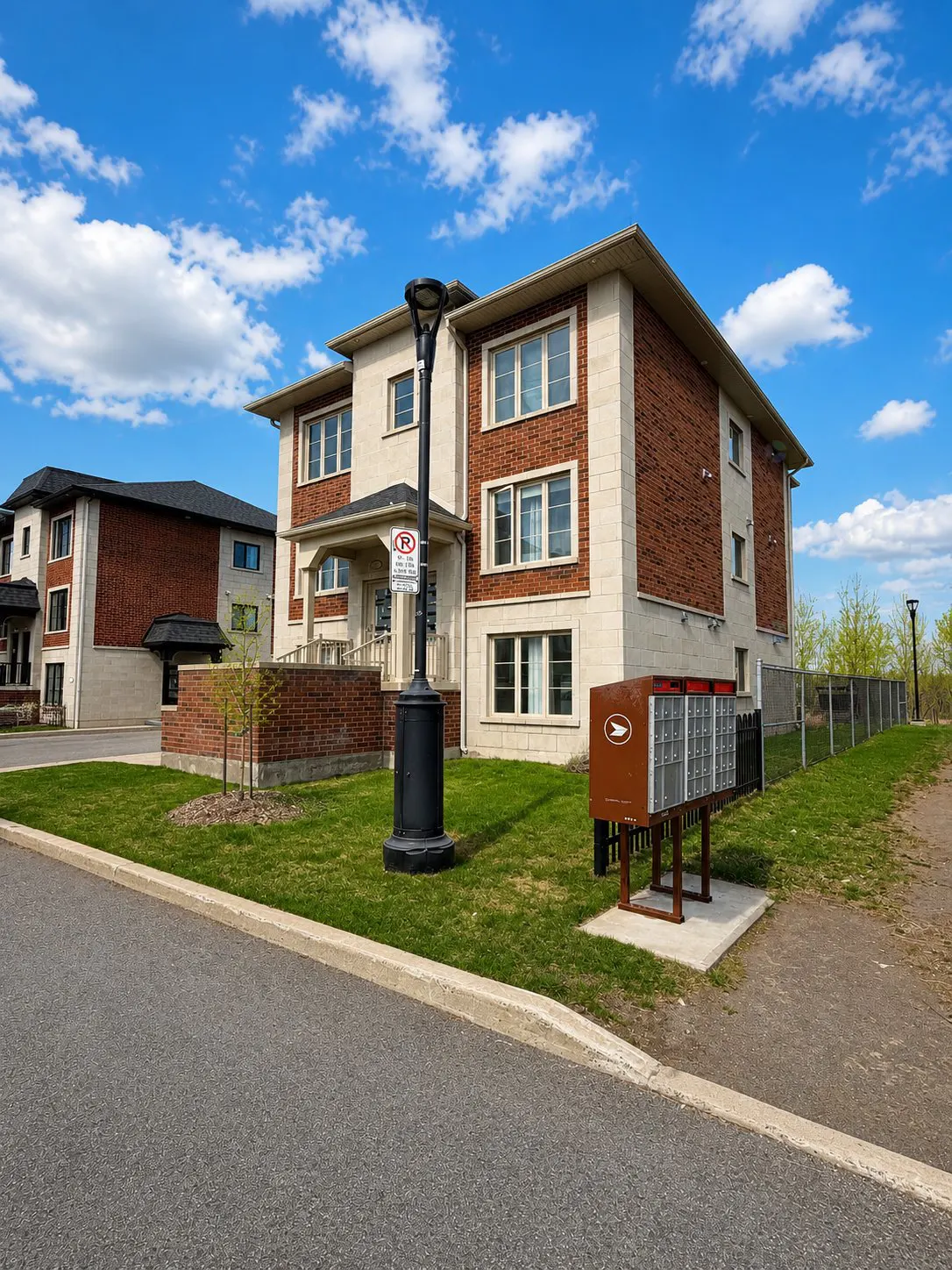 Two-story apartment building with brick and beige siding, a black lamppost, and a brown mailbox stand on a green lawn.