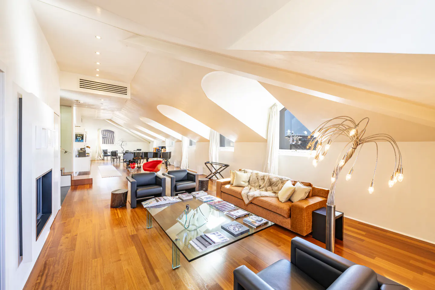 Bright, modern attic living room with wood floors, white walls, and a brown sofa. A glass coffee table sits in the center.