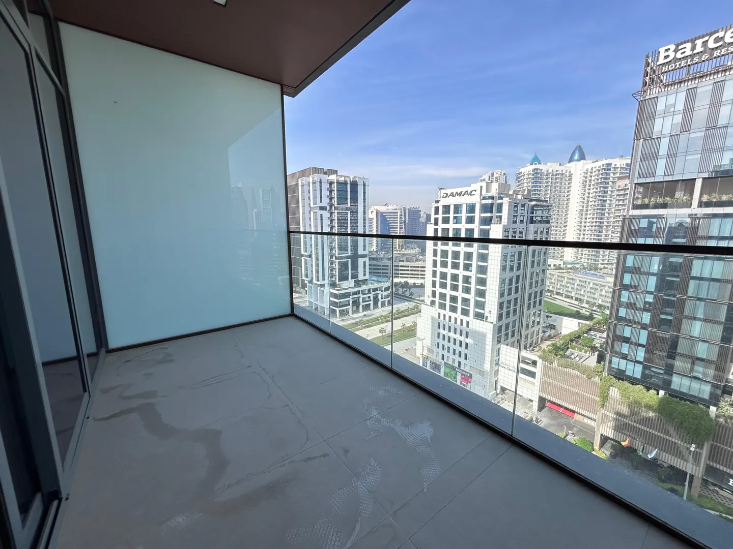 Balcony view of a city skyline with modern buildings under a blue sky. Glass railings and tiled floor.