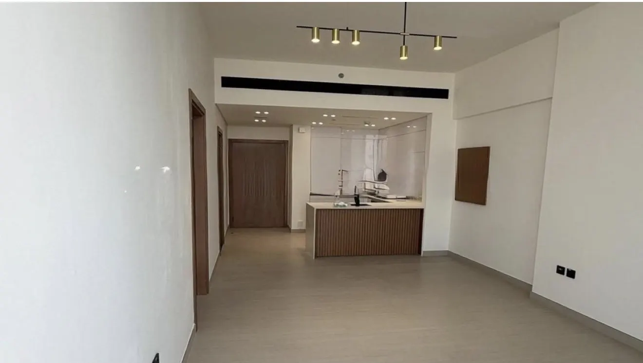 An interior view of a modern apartment with white walls, a small kitchen area, and a light fixture.
