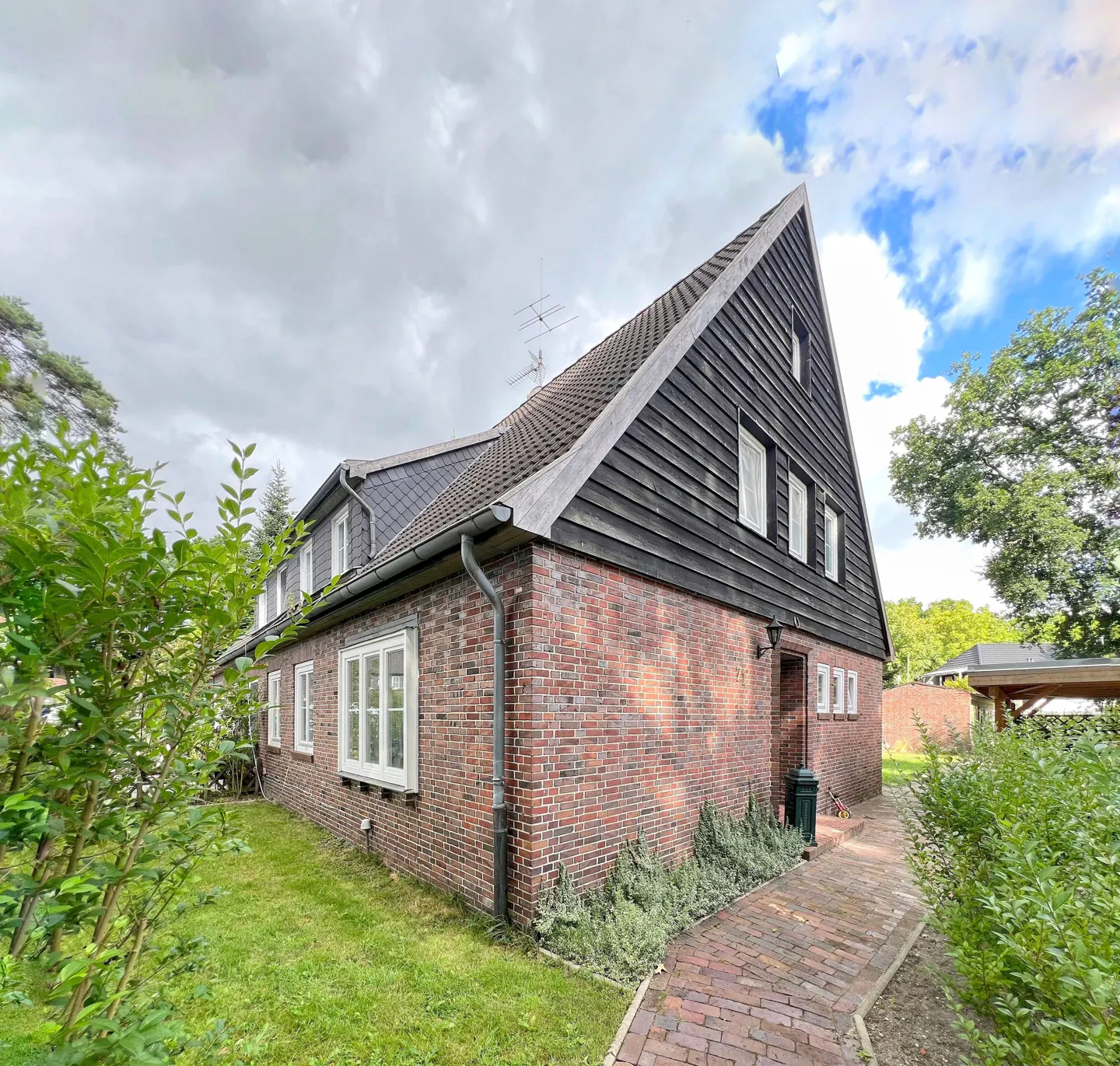 Exterior view of a brick house with a dark wood gable, white windows, and a brick path leading to the entrance.