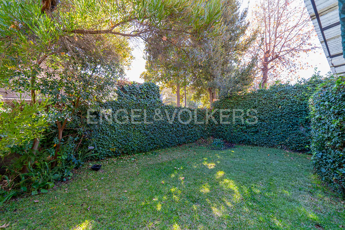 A green lawn is surrounded by a tall, ivy-covered hedge and trees. The Engel & Volkers logo is superimposed on the hedge.