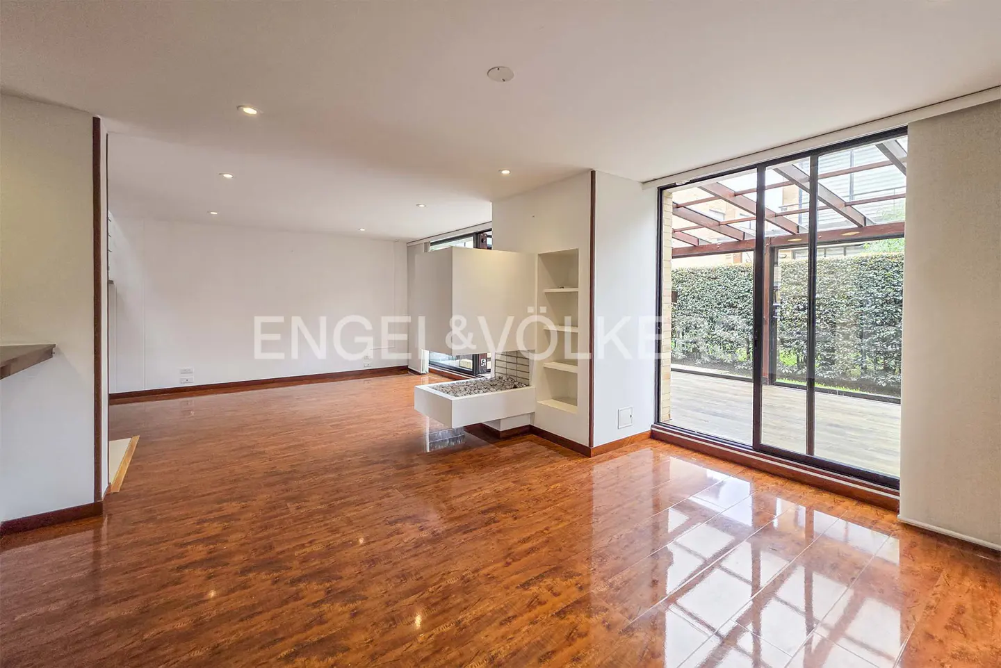 Bright, empty living room with hardwood floors, white walls, and a modern white fireplace. Large sliding glass doors lead to an outdoor patio.