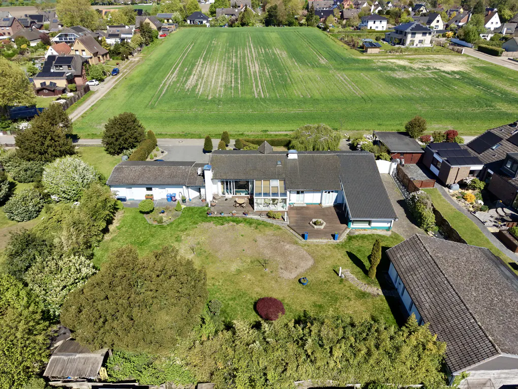 Aerial view of a white house with a gray roof, a large green field in the background, and trees surrounding the property.