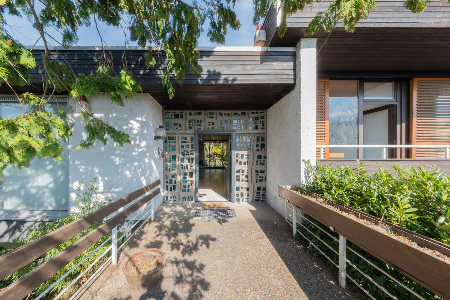 Exterior view of a modern home's entrance with a concrete walkway, decorative teal block wall, and wood accents.