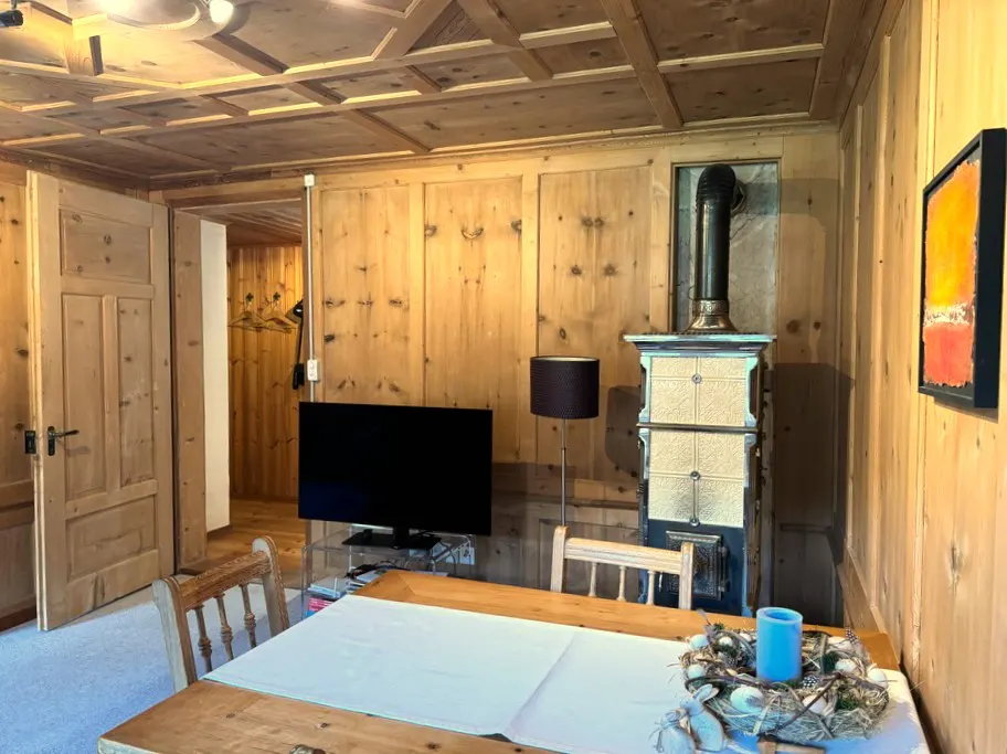 Living room with wood paneled walls, ceiling, and door. A wood table with white tablecloth and a fireplace are also visible.