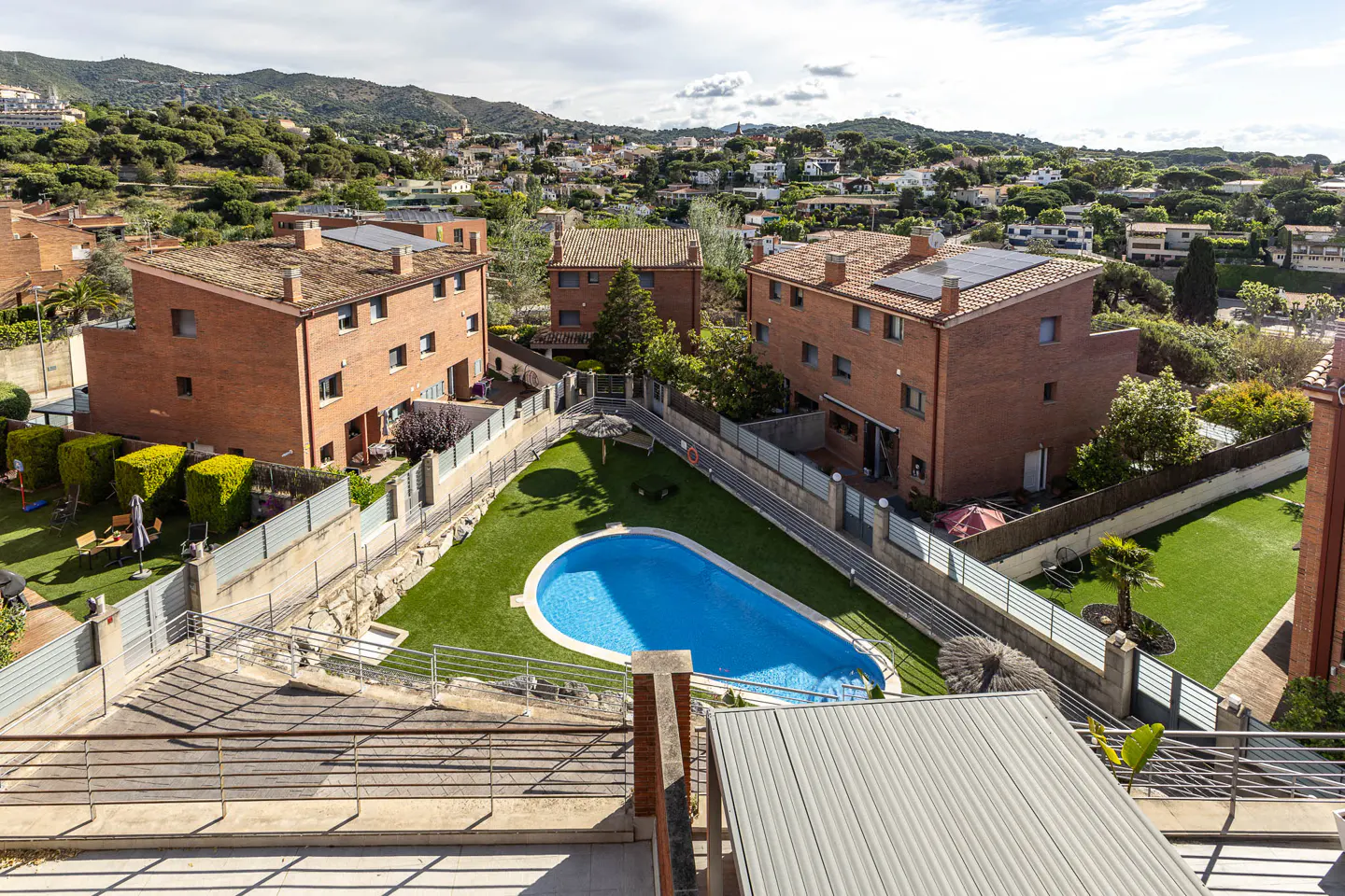 Aerial view of red brick townhouses surrounding a blue pool and green lawn, with a mountain backdrop.