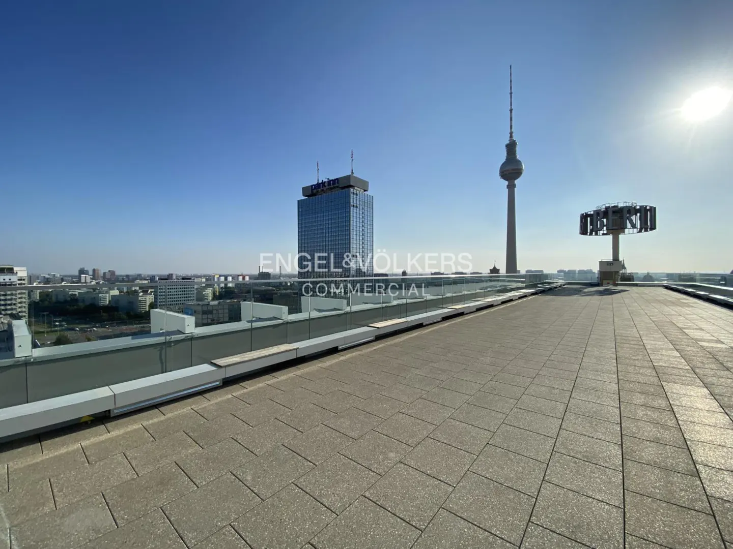 Rooftop view of Berlin with the TV Tower and Park Inn Hotel in the background. The terrace has a glass railing and gray paving.