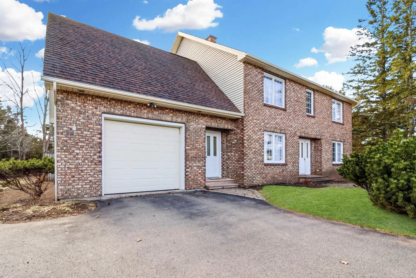 Two-story brick house with a brown roof, white garage door, and white front doors under a blue sky.