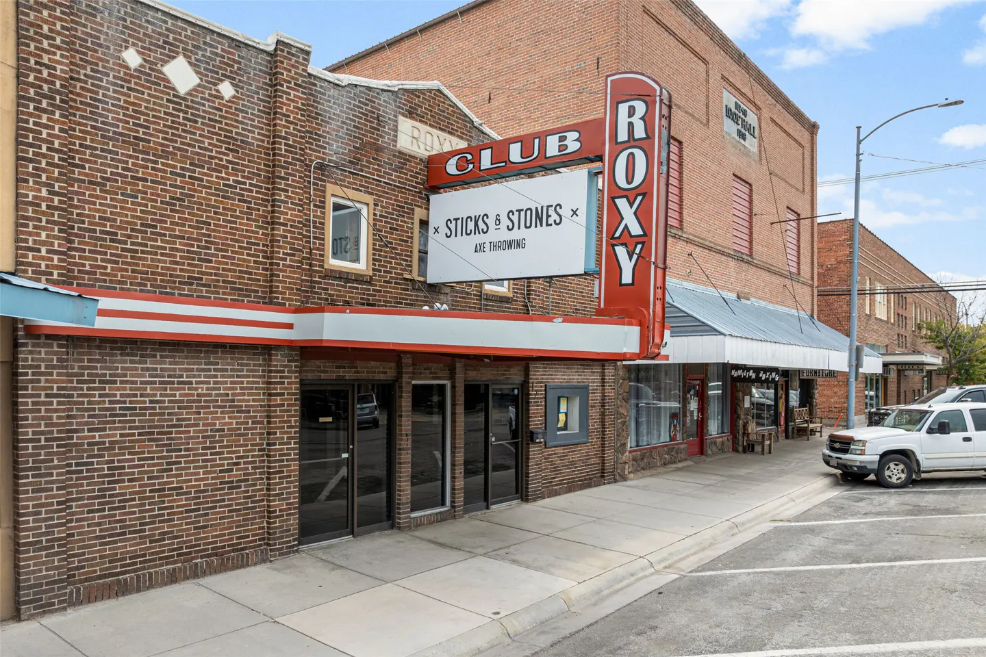Exterior view of the Club Roxy, a brick building with a red neon sign, advertising "Sticks & Stones Axe Throwing".