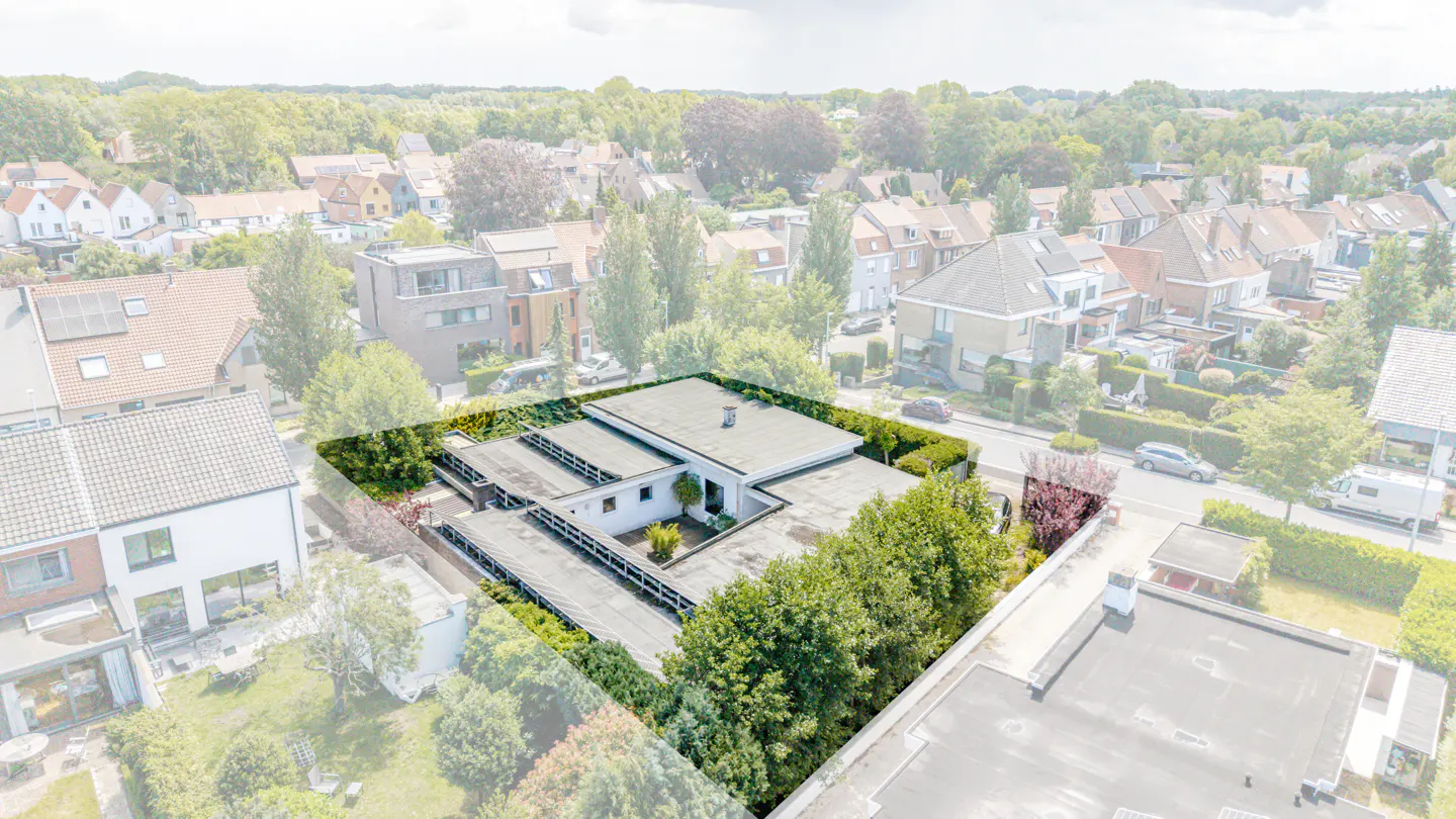 Aerial view of a modern flat-roofed house surrounded by lush green hedges in a quiet residential neighborhood.