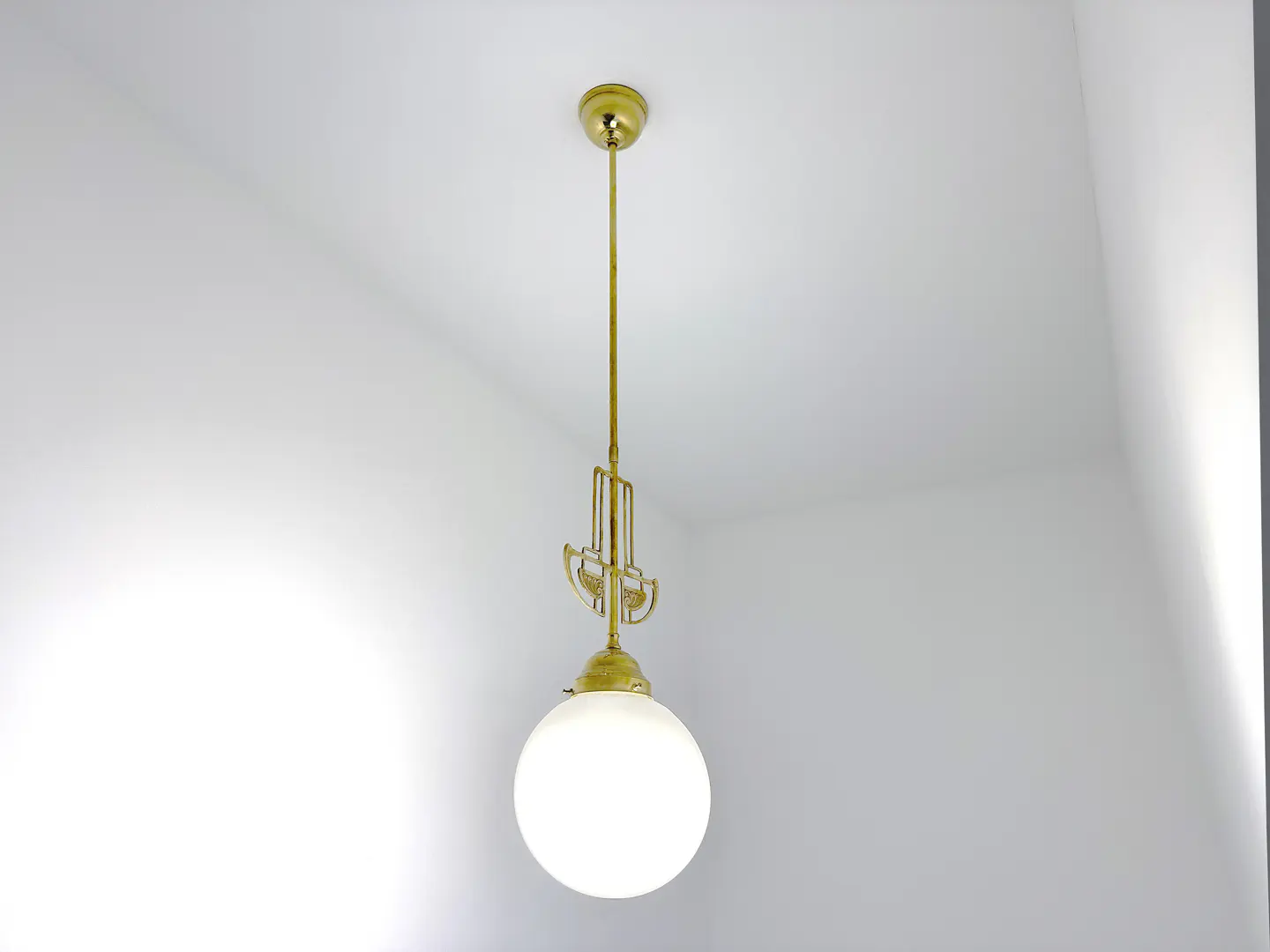 A gold pendant light fixture hangs from a white ceiling. The light has a round, white glass shade.