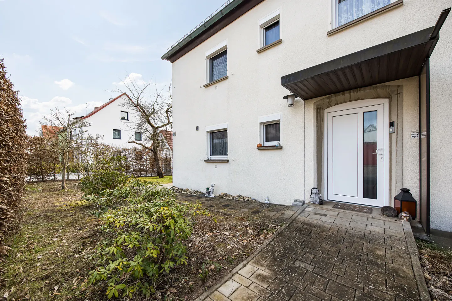 Exterior of a two-story white house with a white front door and a stone walkway leading up to it. A garden is on the left.