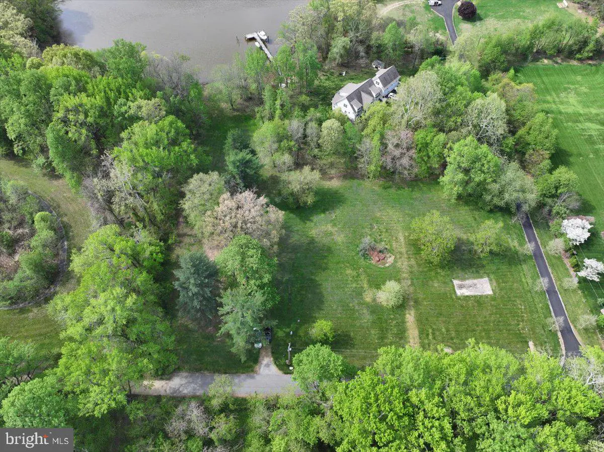 Aerial view of a property with a house, dock, lake, and green trees.