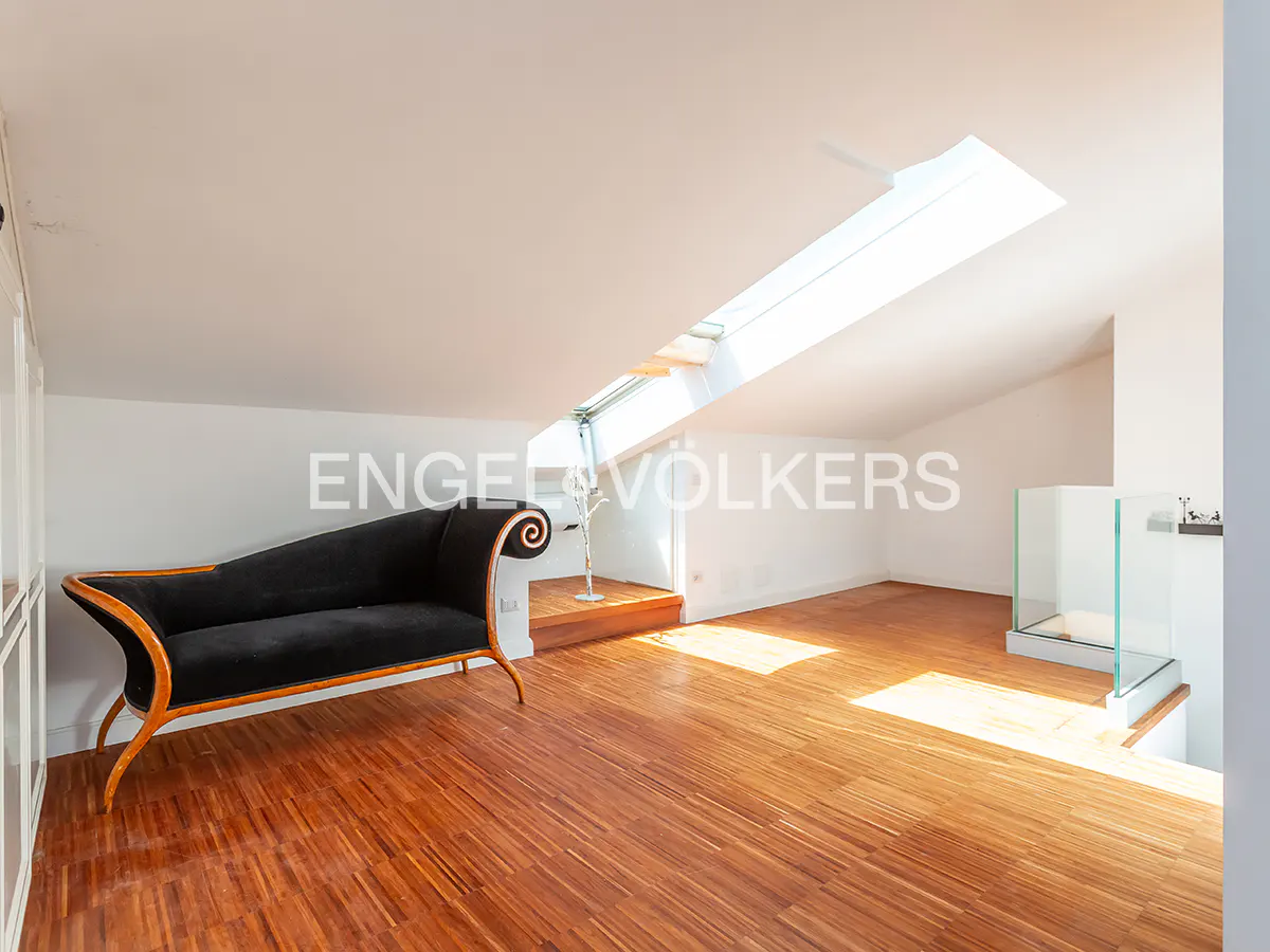 Attic room with wood floors, skylight, and black chaise lounge. Engel & Völkers logo on the wall.