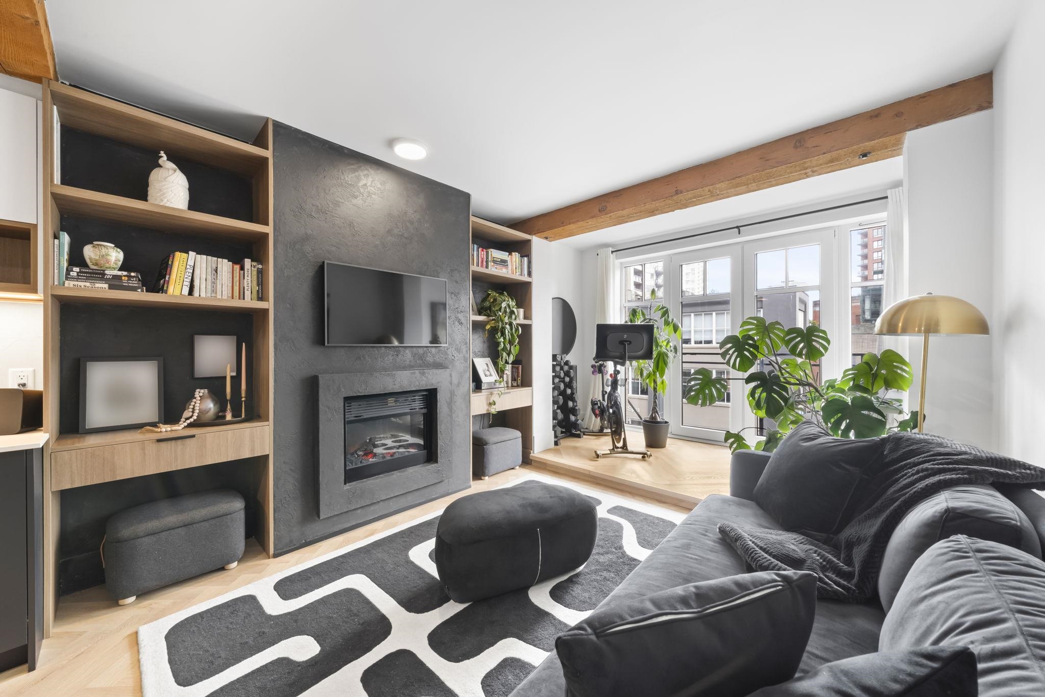 Living room with gray sofa, black and white rug, fireplace, TV, and bookshelves. Exercise bike visible near patio doors.