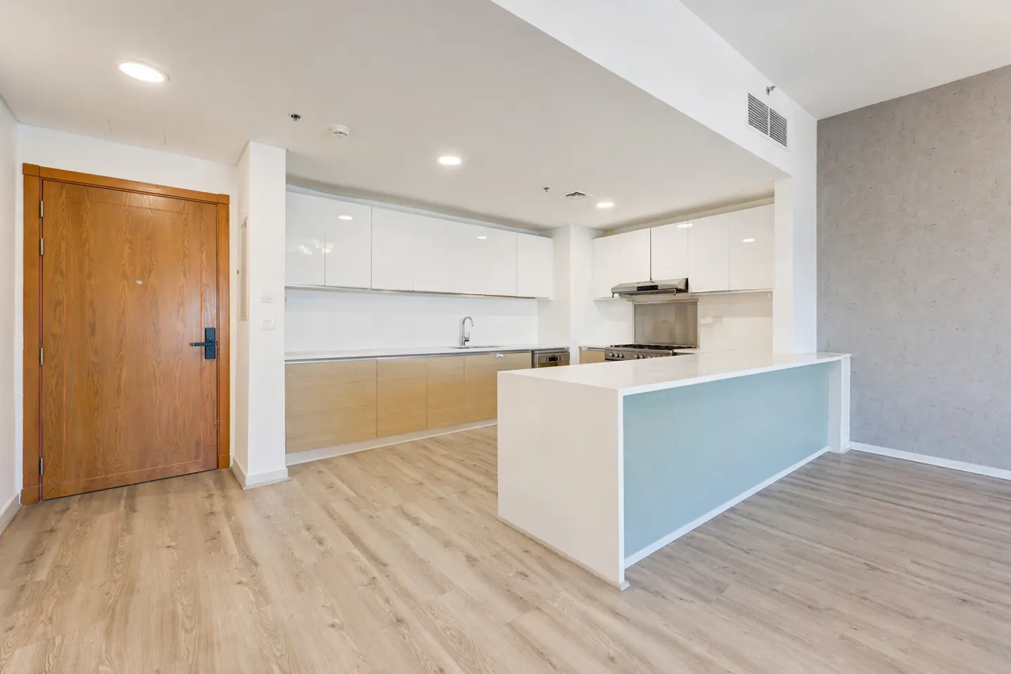 A bright, modern kitchen with white cabinets, light wood floors, and a blue-accented island. A wooden door is on the left.