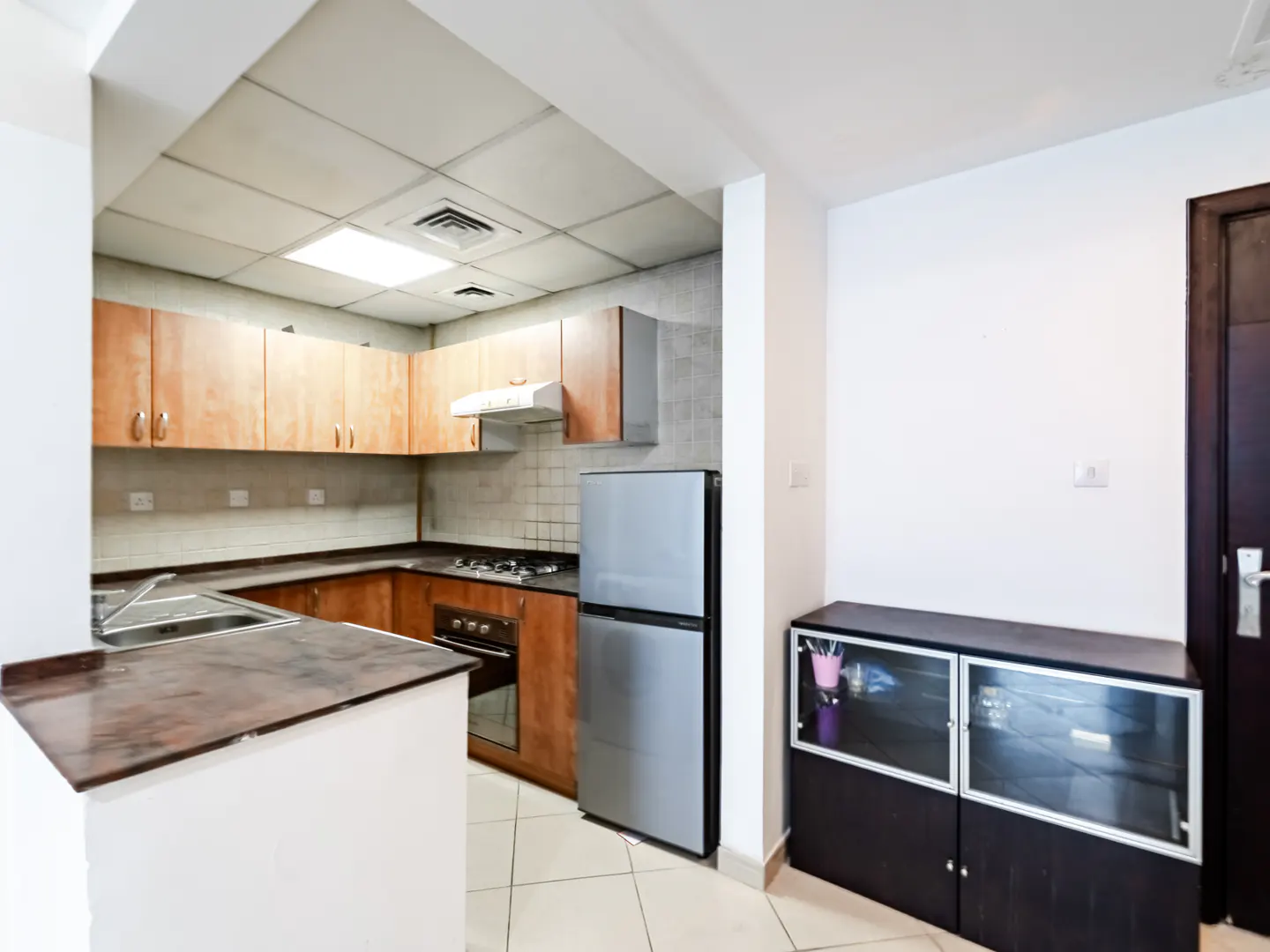 Kitchen with wooden cabinets, stainless steel appliances, a dark countertop, and a black glass-fronted storage cabinet.