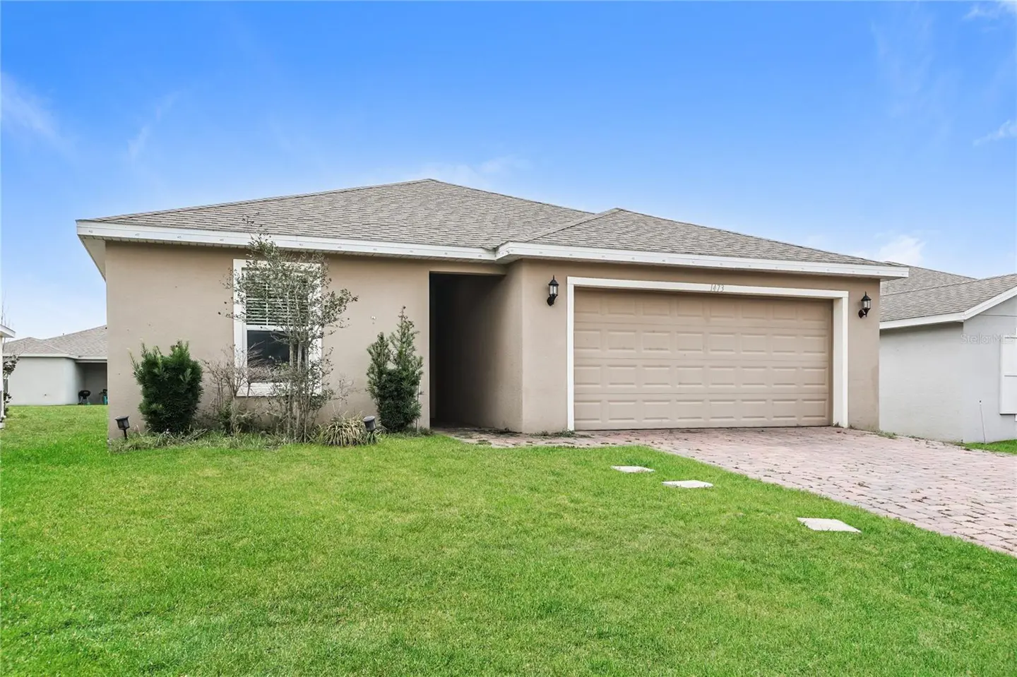 Beige single-story house with a gray roof, a two-car garage, and a green lawn under a blue sky.