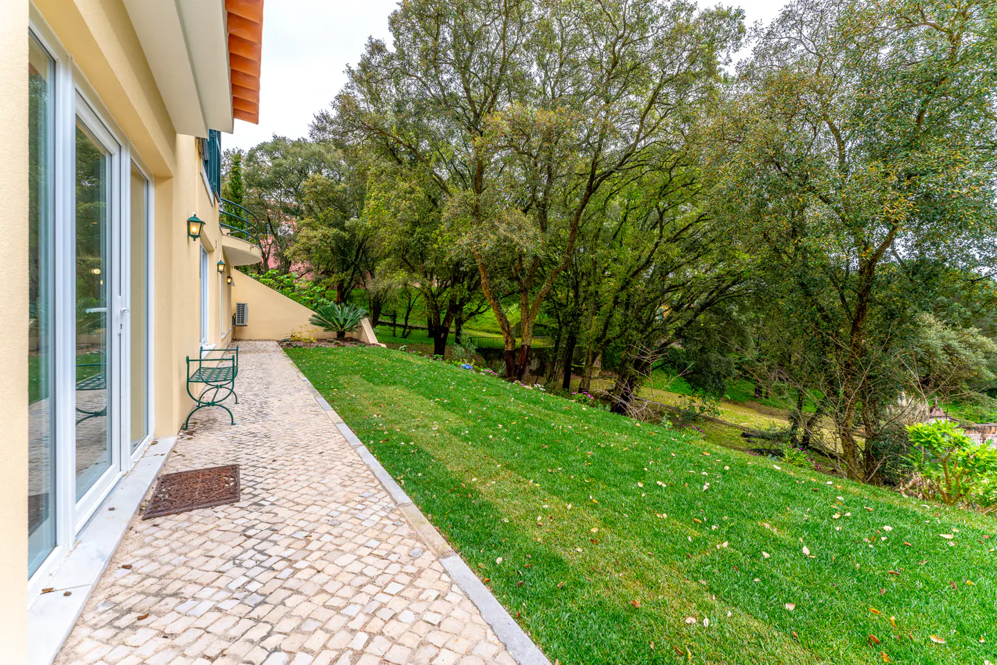 Exterior view of a yellow house with a stone patio, green lawn, and trees.