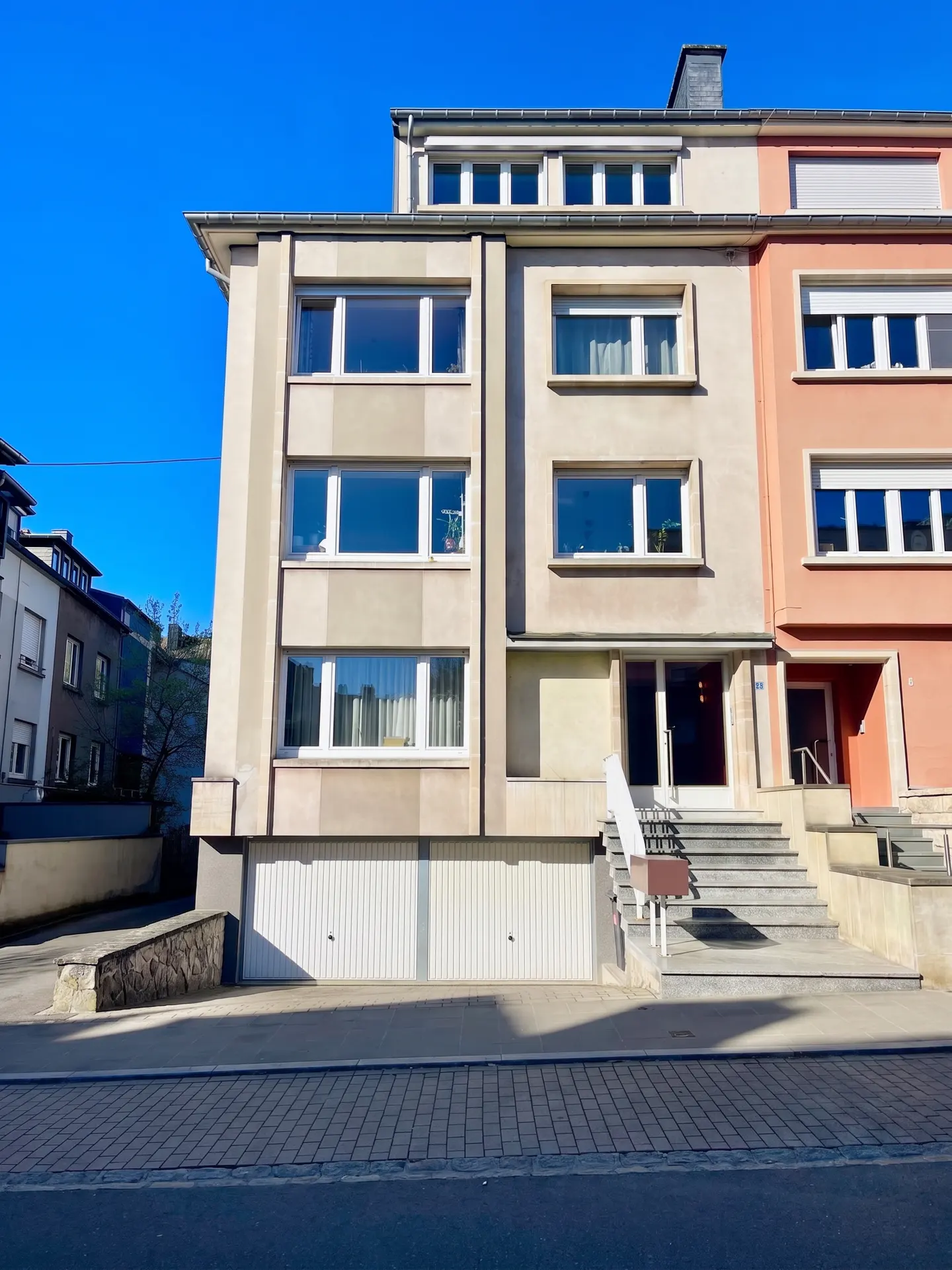 Three-story apartment building with a garage, steps to the front door, and large windows under a clear blue sky.