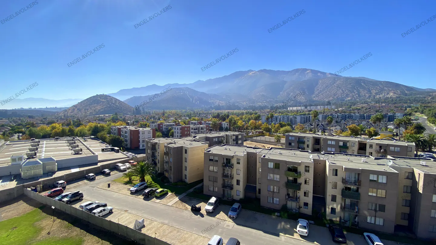 A sunny, wide shot of apartment buildings and cars with mountains in the background.