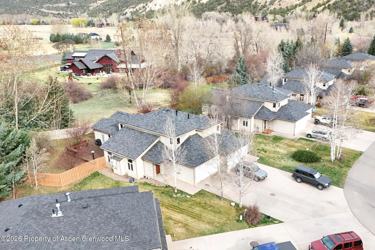 Aerial view of beige houses with gray roofs, cars in driveways, and trees in a mountain setting.