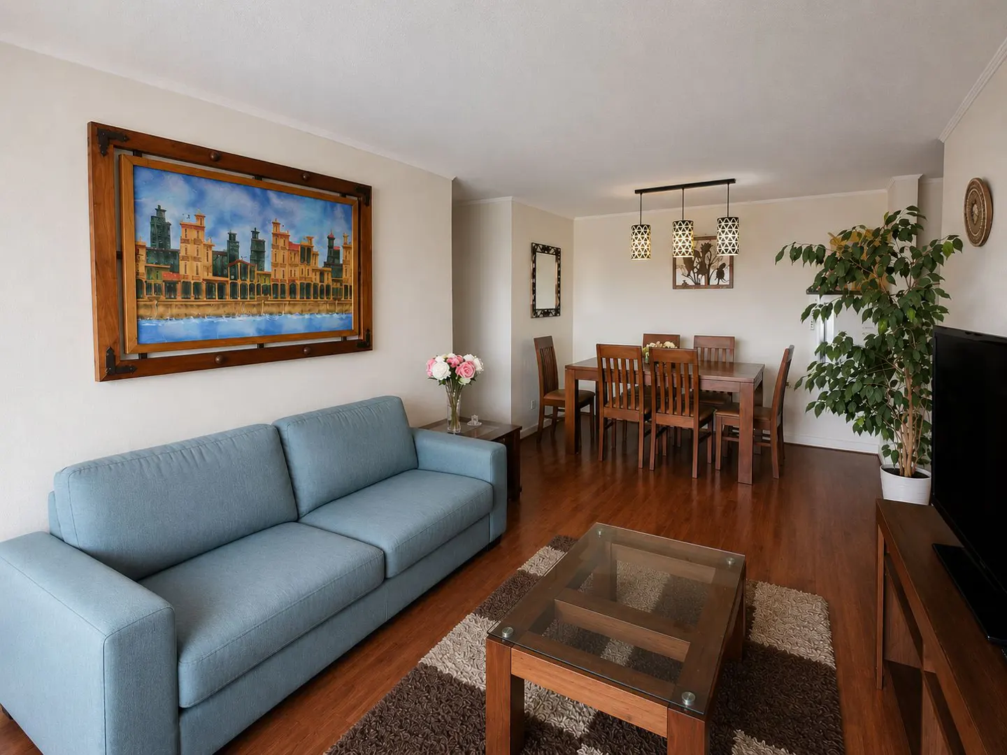 Living room with a blue sofa, a painting, a dining table with chairs, and a coffee table on a brown rug.