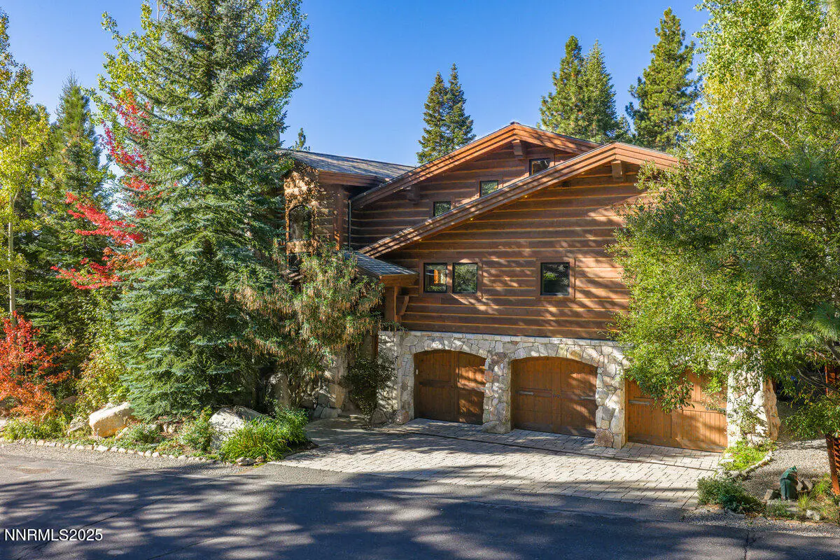 Exterior view of a log cabin home with a stone garage, surrounded by green trees and a blue sky.