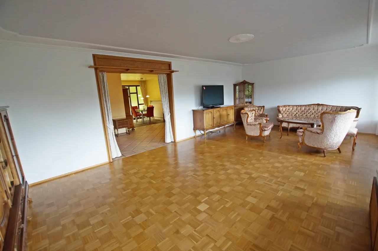 Living room with parquet floors, white walls, and antique furniture. A dining room is visible through an open doorway.