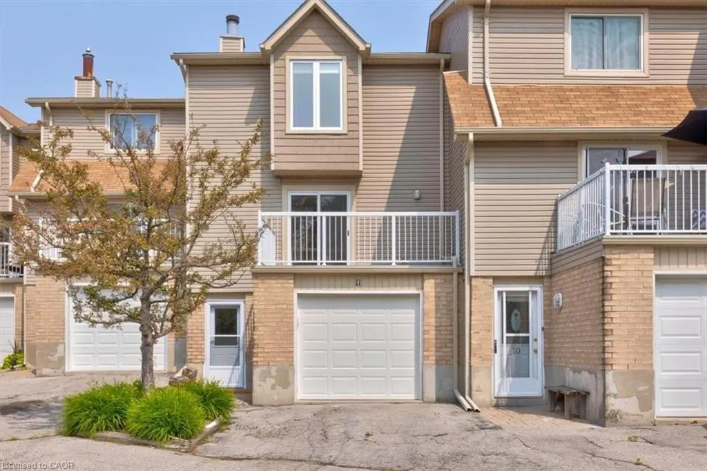 Tan townhouse with white garage door, balcony, and trim. A small tree is in front of the building.