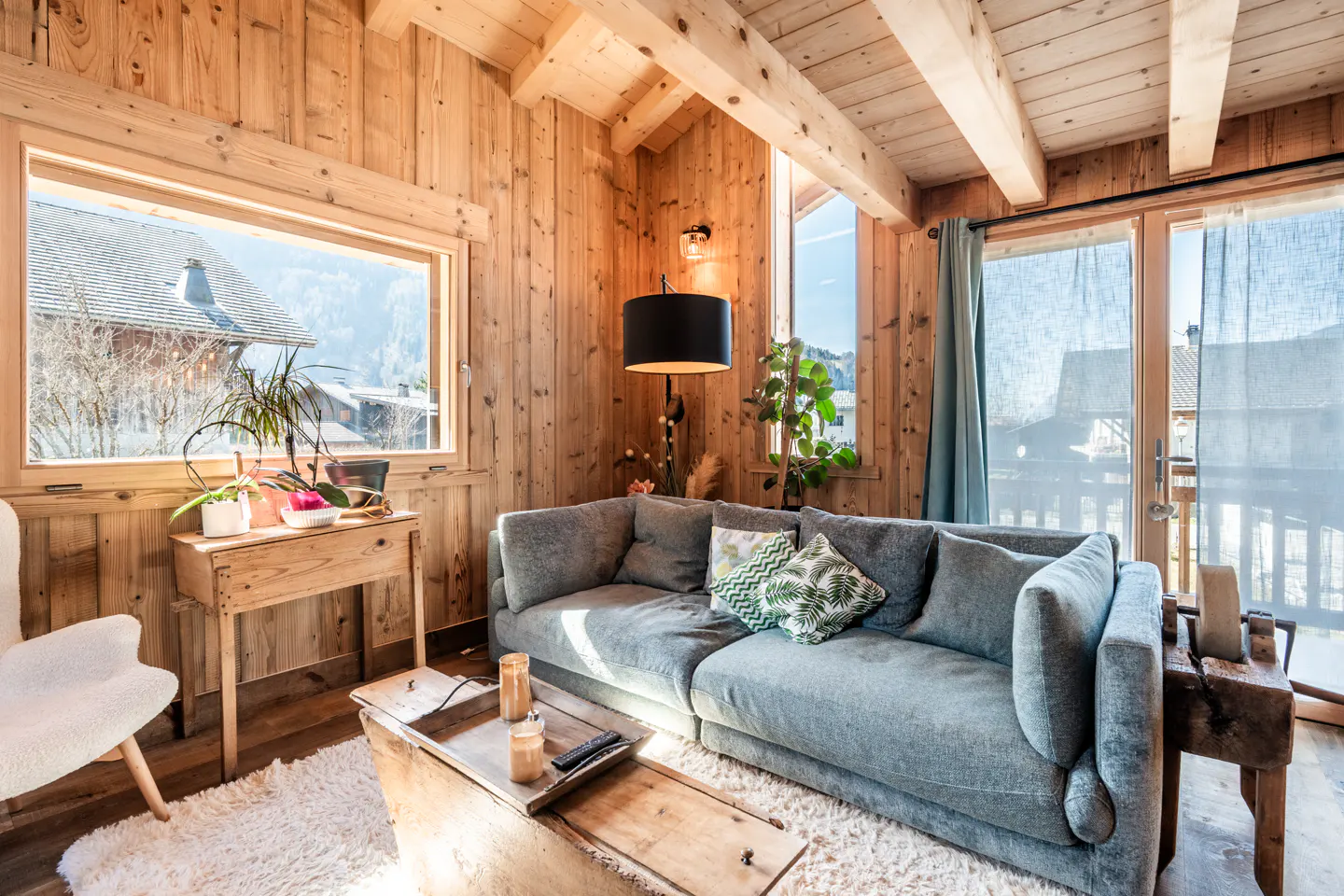 Cozy living room with wood paneled walls, a gray sofa, and a view of the mountains through a large window.