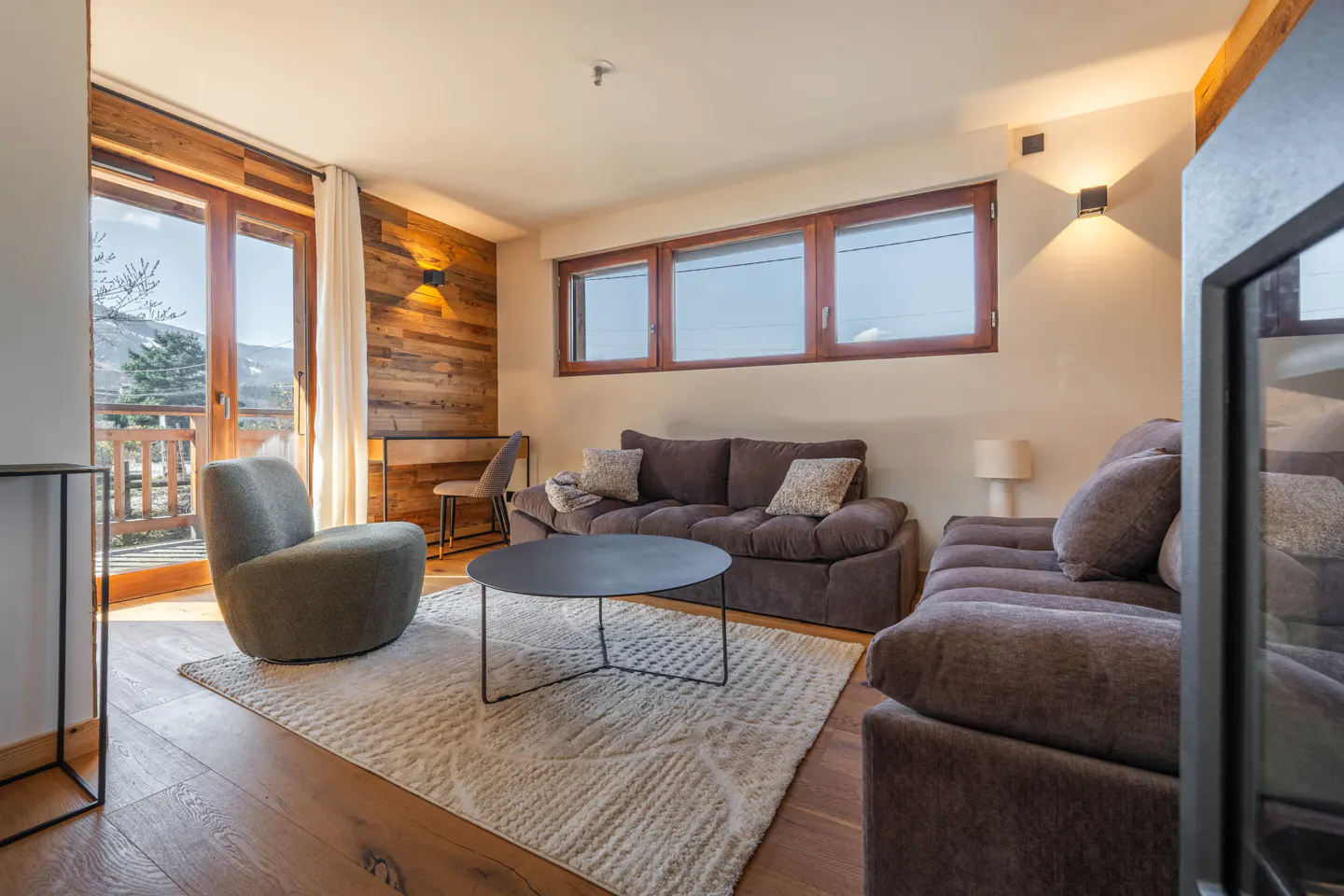 Living room with brown sofas, a round black table on a patterned rug, and a view of mountains through a glass door.